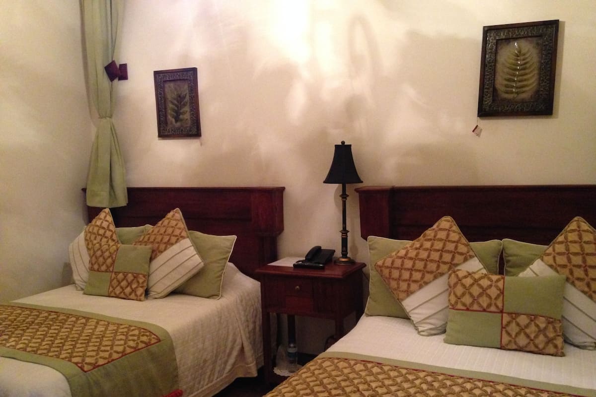 Une chambre d’hôtel avec deux lits, une table de chevet avec une lampe et un cadre décoratif représentant une feuille accroché au mur.