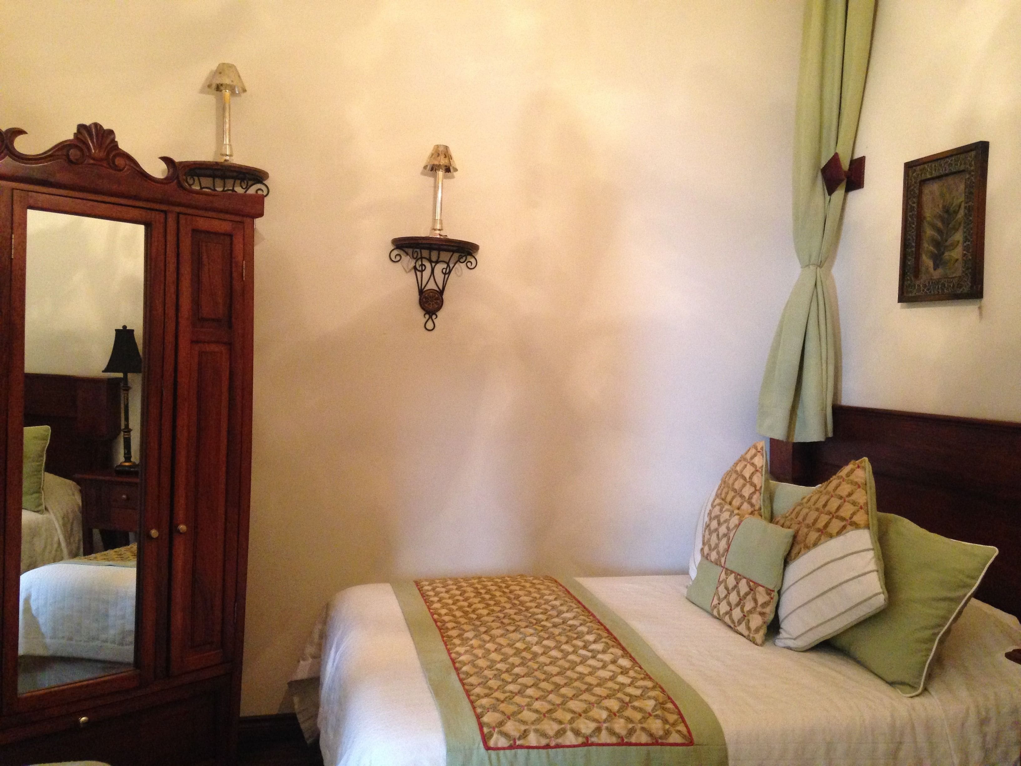 A bedroom with a bed, a wooden wardrobe, a wall-mounted lamp, and a mirror.