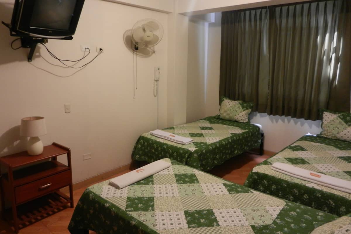 Quarto de hotel com duas camas, uma televisão fixada na parede, uma mesa de cabeceira com abajur e uma janela com cortinas.