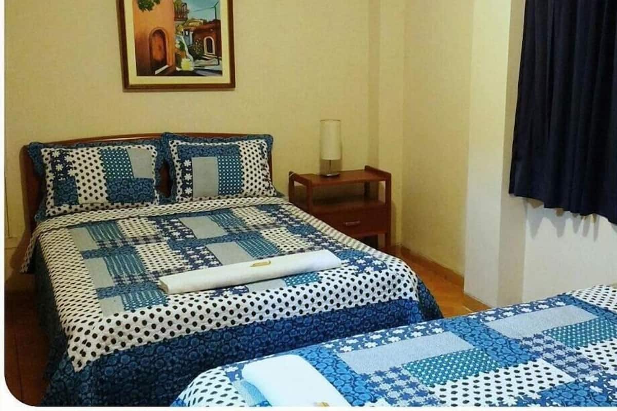 Quarto com duas camas, mesa de cabeceira, luminária e um quadro na parede.