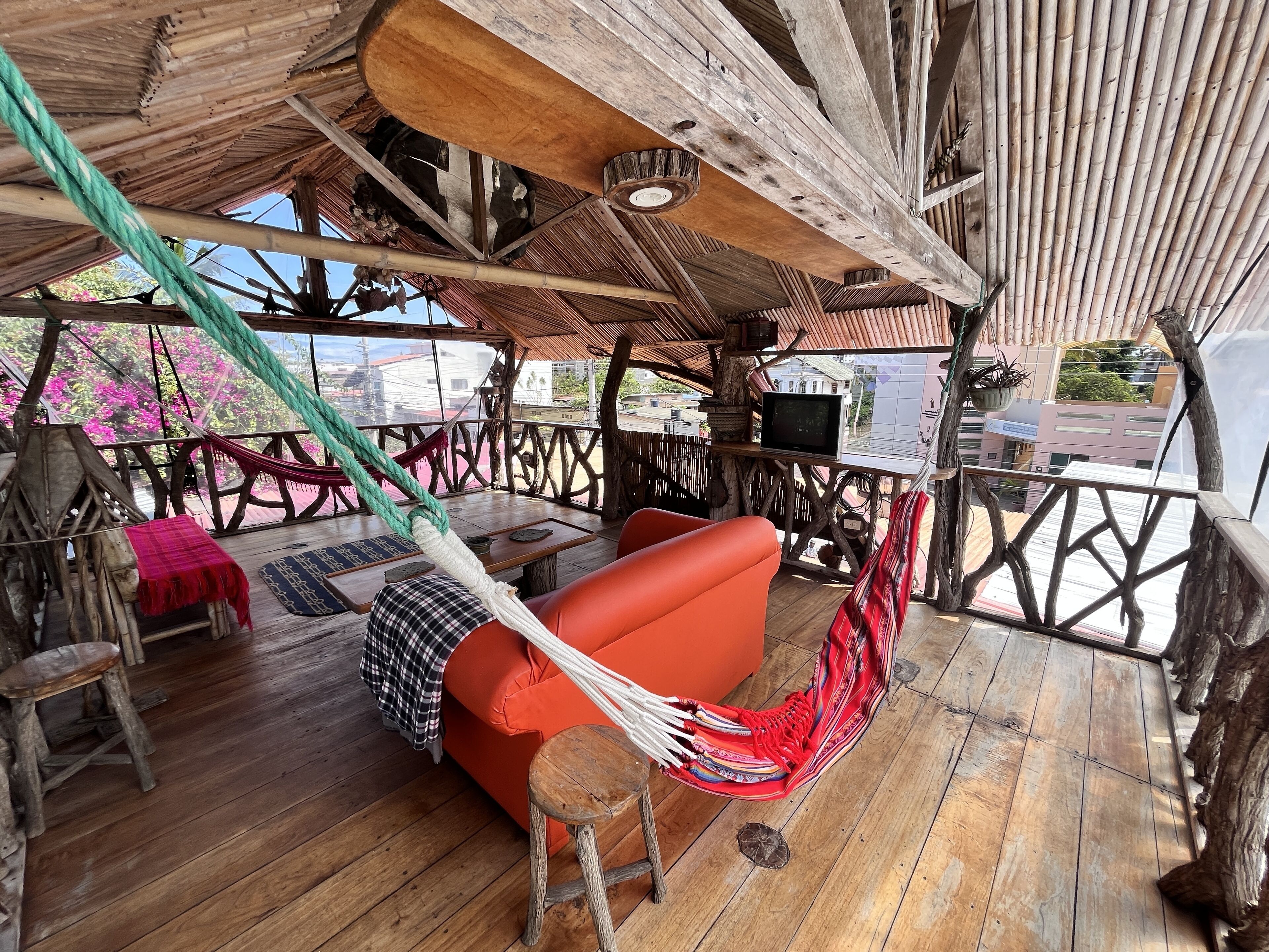 Una terraza de madera con una hamaca, un sofá rojo y un televisor sobre una mesa.
