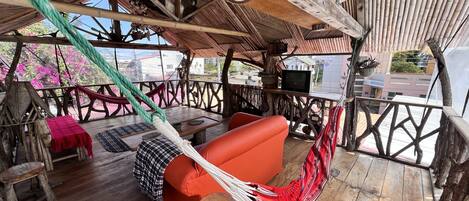 Una terraza de madera con una hamaca, un sofá rojo y un televisor sobre una mesa.