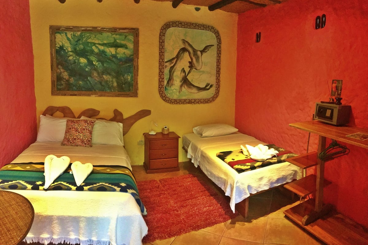 A room with two beds, a red rug, a wooden nightstand, a TV, and artwork on the walls.