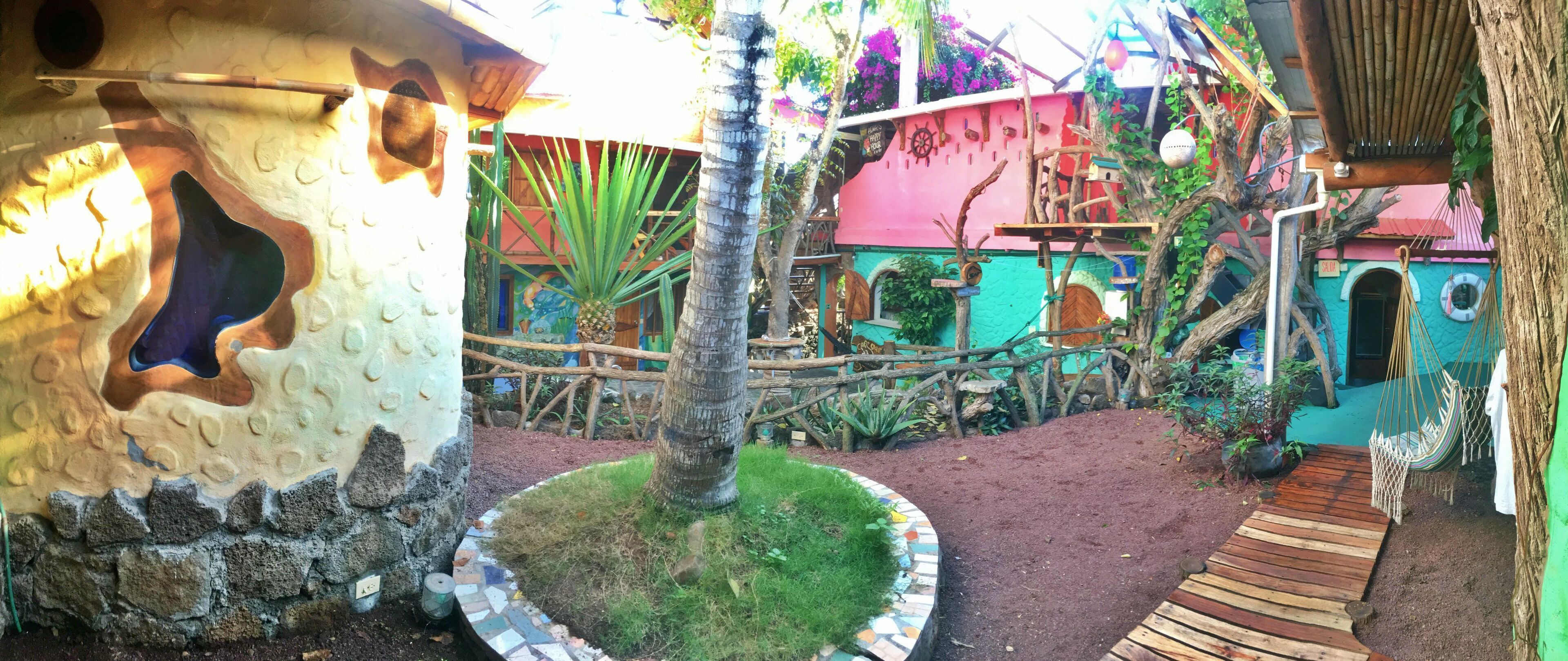 Un jardín tropical con una terraza de madera, una palmera y un parque infantil colorido.