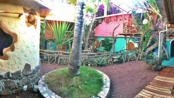 Un jardín tropical con una terraza de madera, una palmera y un parque infantil colorido.