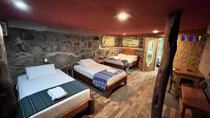 A rustic room with two wooden beds, a stone wall, and a wooden table. - Lonesome George Ecolodge (Puerto Ayora)
