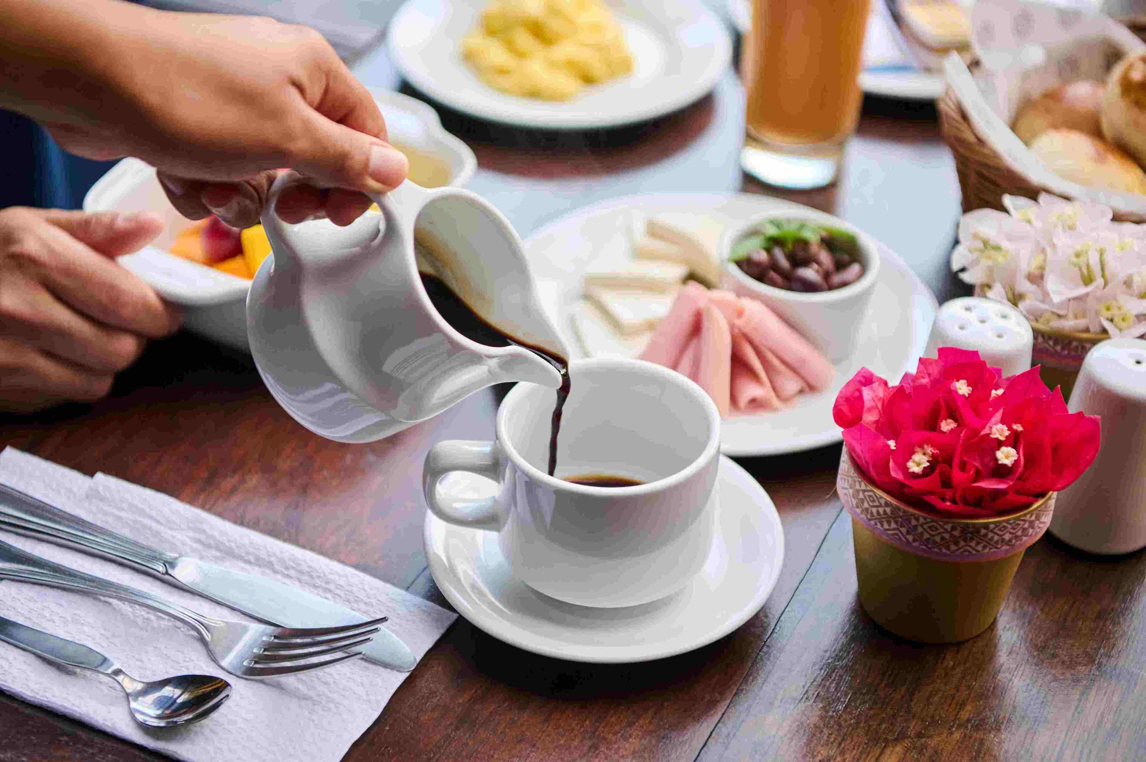 A dining table with a cup of coffee, a plate of food, and a salt and pepper shaker.