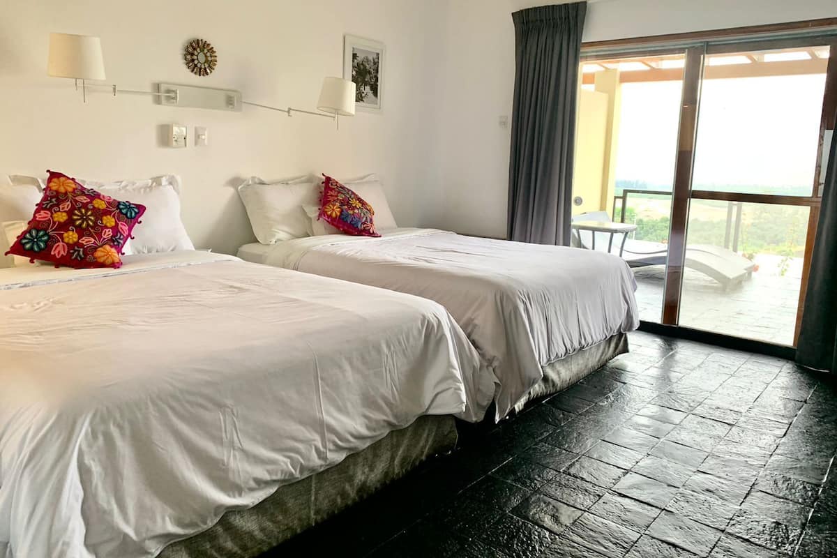 A hotel room with two beds, a large window with a view, and a balcony.