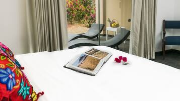 Une chambre d’hôtel avec un lit, une fenêtre avec des rideaux, une petite table sur laquelle se trouve un panier de fruits, et une chaise.