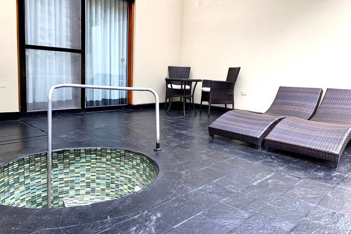 A spa area with a hot tub, wicker lounge chairs, and a table with chairs.