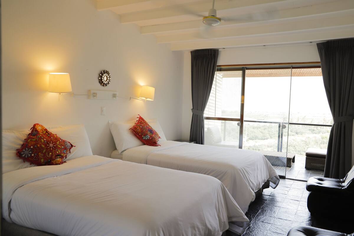 A hotel room with two beds, a sofa, a ceiling fan, and a large window with curtains.