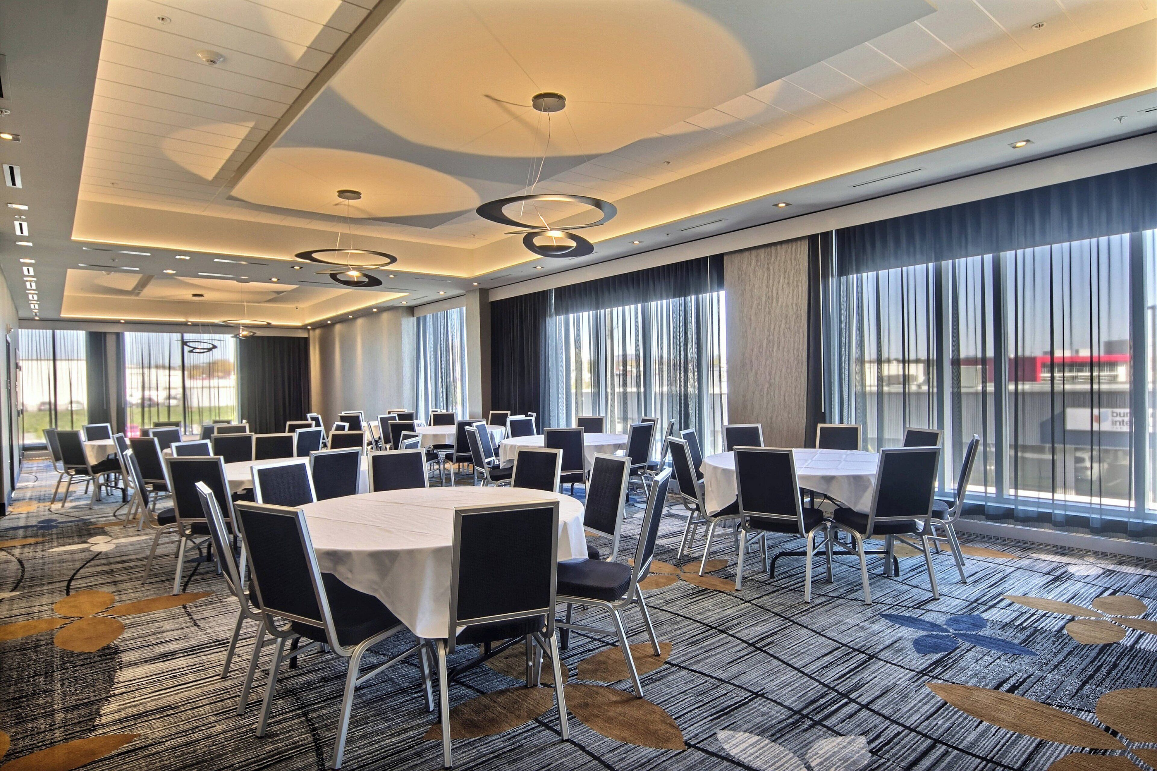 A conference room with multiple tables and chairs, large windows with curtains, and a patterned carpet.