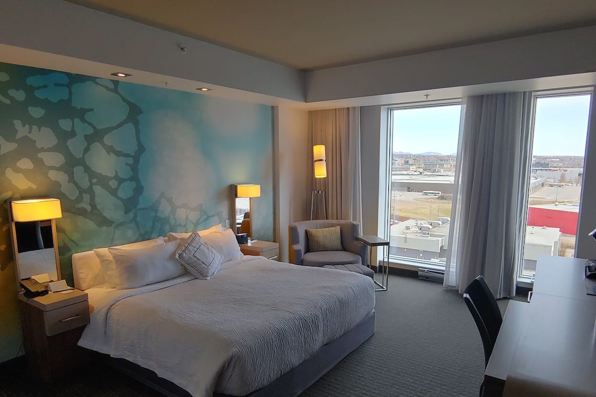 Habitación de hotel con una cama grande, un escritorio, una silla y vistas al aeropuerto.