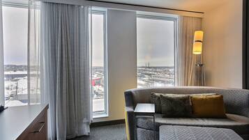 A modern hotel room with a large window, a sofa, a small table, and a floor lamp.