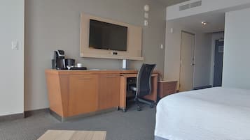Una habitación de hotel con una cama, un escritorio con una silla, un televisor y una cafetera.