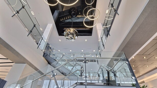 Un interior moderno con una escalera de cristal, barandillas metálicas y un aplique decorativo.