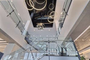 Un interior moderno con una escalera de cristal, barandillas metálicas y un aplique decorativo.