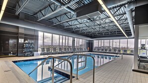 Una piscina interior con agua cristalina, barandales de metal y vistas a la ciudad a través de amplias ventanas.
