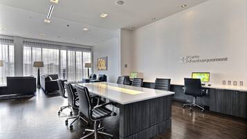 A modern conference room with a long table, several chairs, and a desk with a computer.