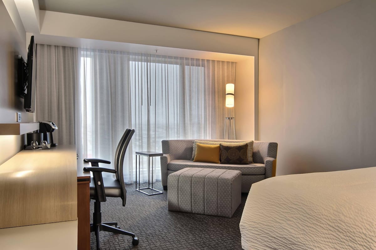 Una habitación de hotel con cama, escritorio, silla, sofá y televisor.