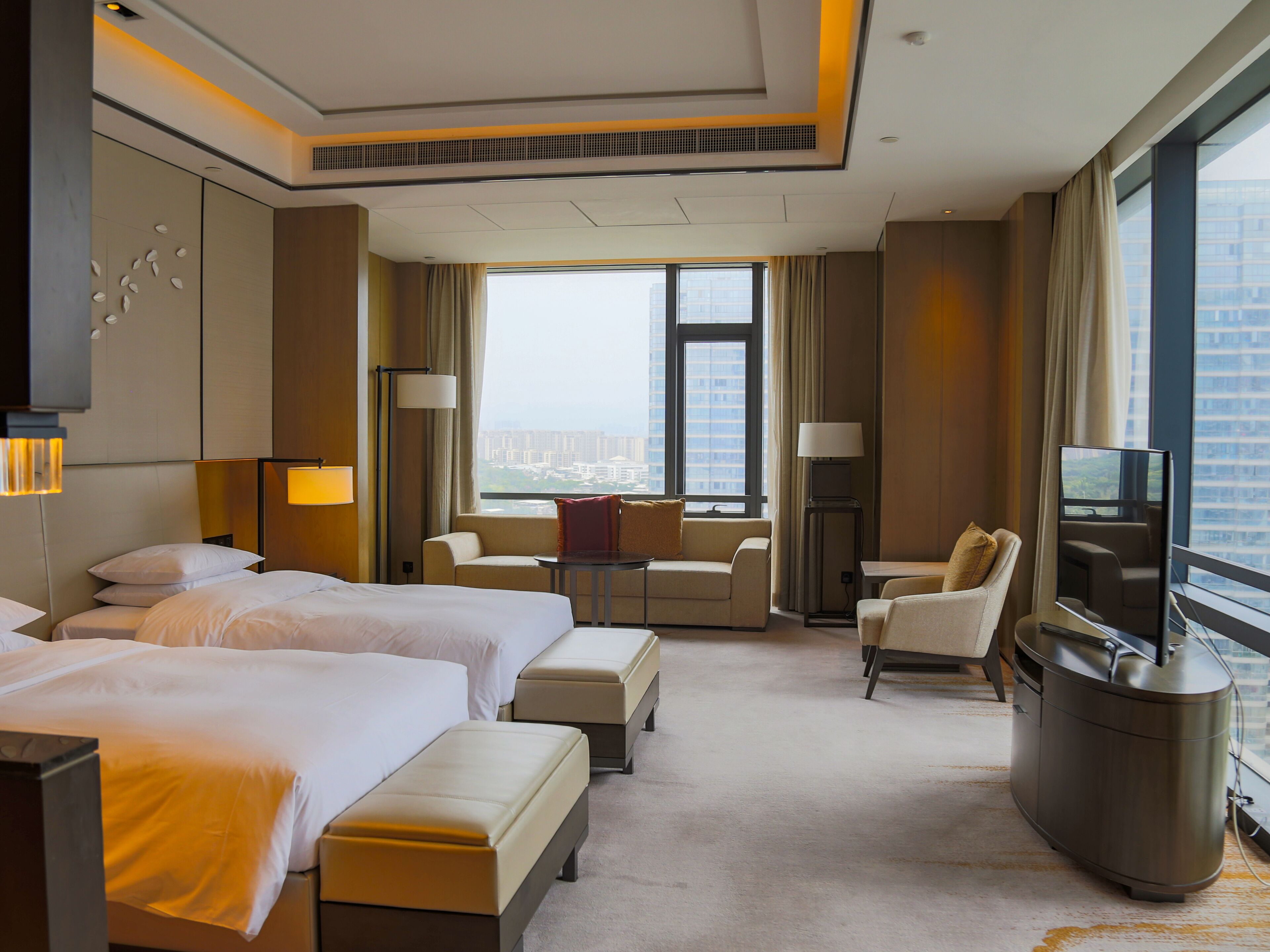A hotel room with two beds, a sofa, a desk, and a TV.