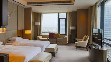 A hotel room with two beds, a sofa, a desk, and a TV.