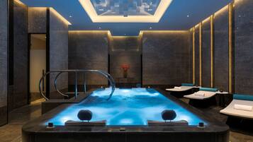 Relax in a serene spa room with a central hot tub and lounge chairs.