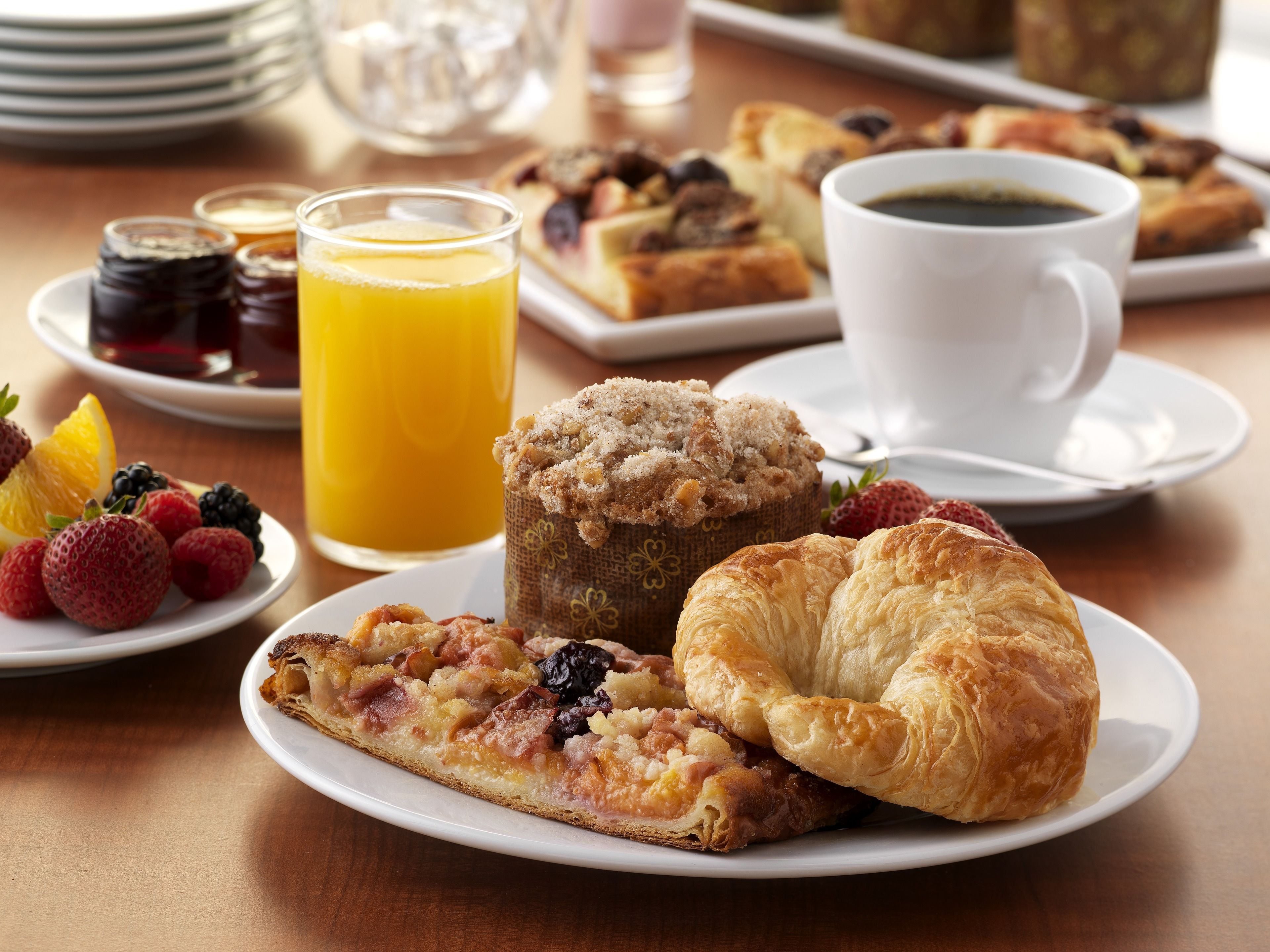 A breakfast setting with pastries, fruits, and beverages on a table.