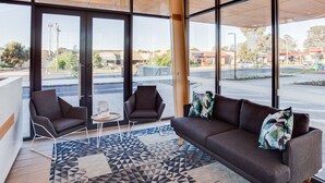 Eine moderne Lobby mit großen Fenstern, einem Sofa, zwei Sesseln und einem gemusterten Teppich.