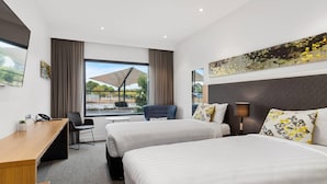 Ein Hotelzimmer mit zwei Betten, einem Schreibtisch, einem Stuhl, einem großen Fenster mit Blick und einem Gemälde an der Wand.