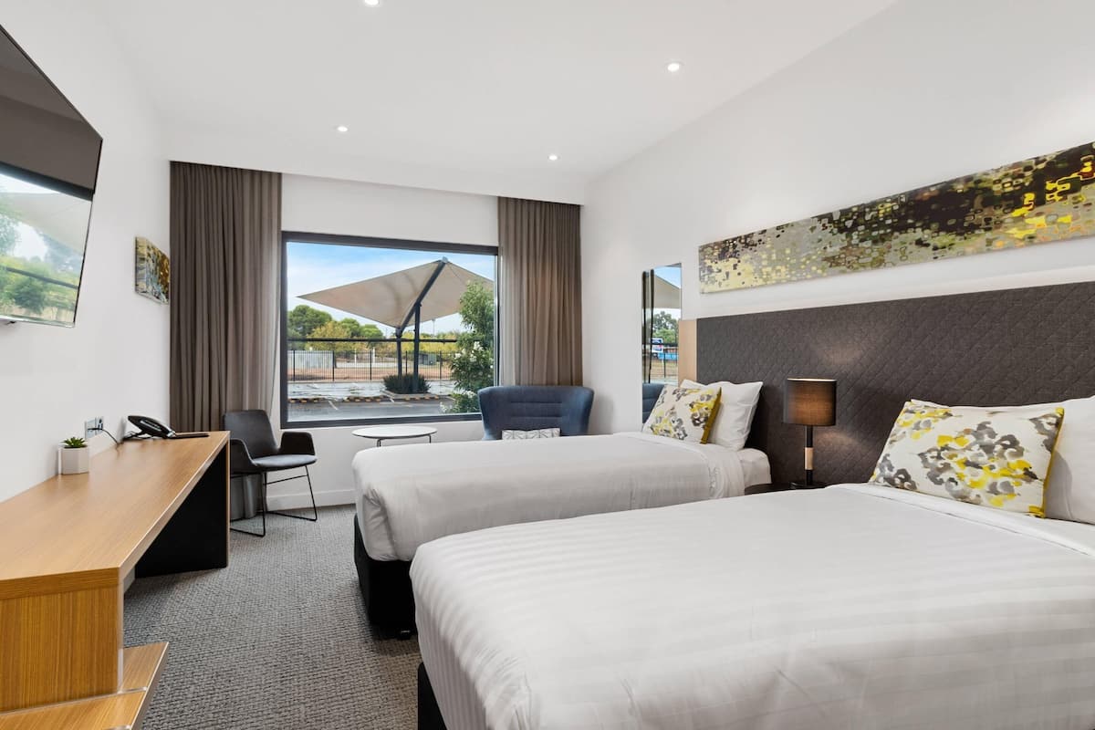 Hotelkamer met twee bedden, een bureau, een stoel, een groot raam met uitzicht en een schilderij aan de muur.