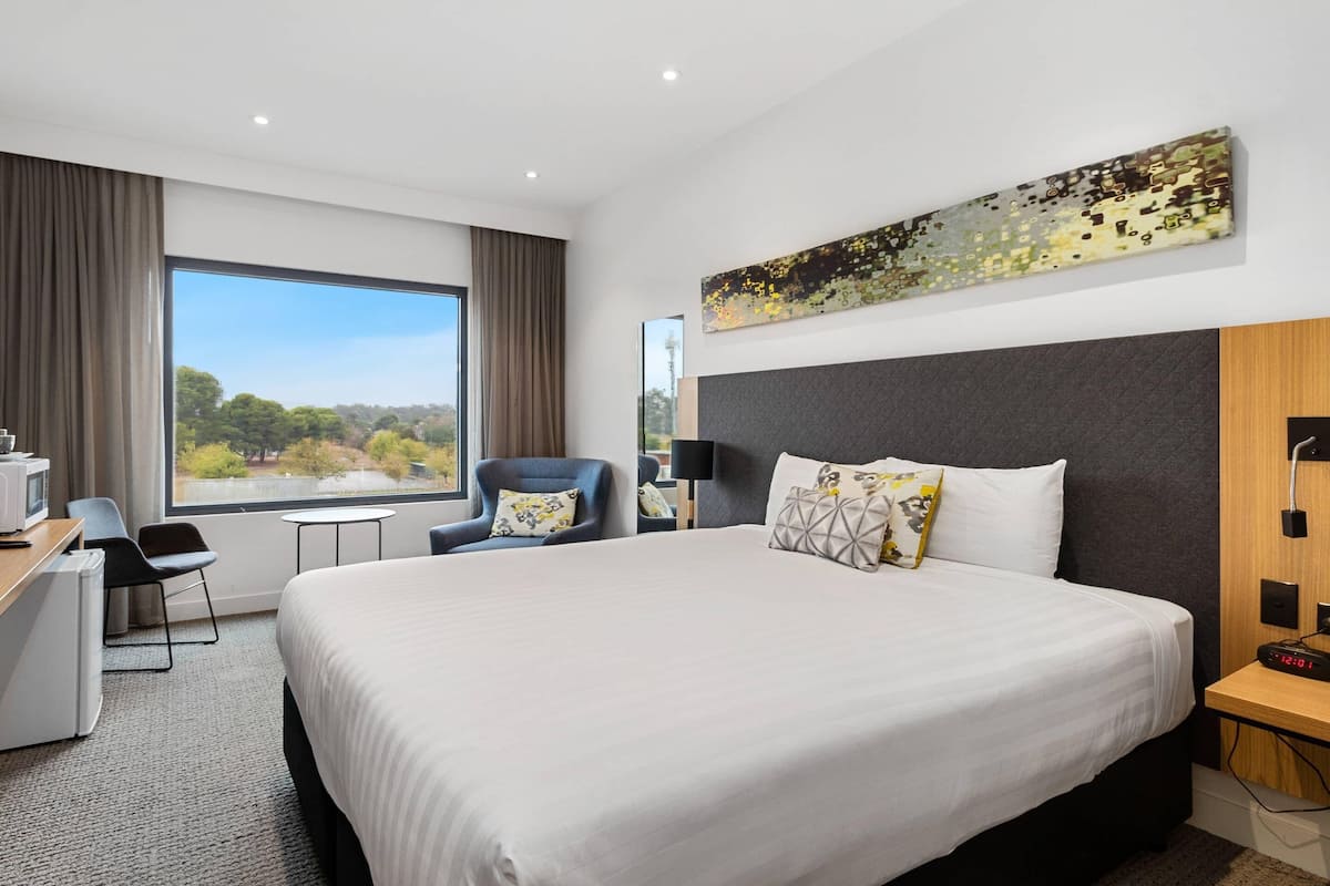 Hotelkamer met een groot bed, een bureau met stoel, een klein tafeltje en uitzicht op het omliggende landschap.