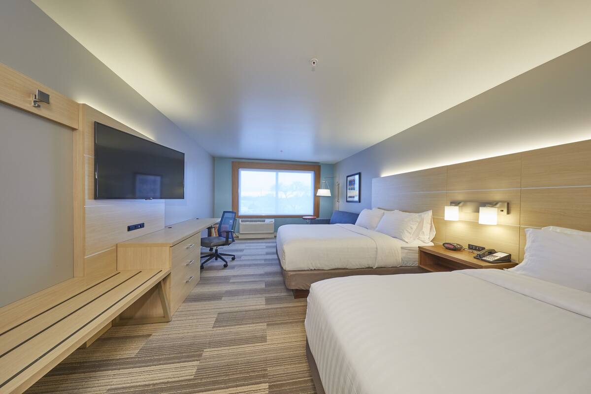 A hotel room with two beds, a desk, a chair, a TV, and a window.