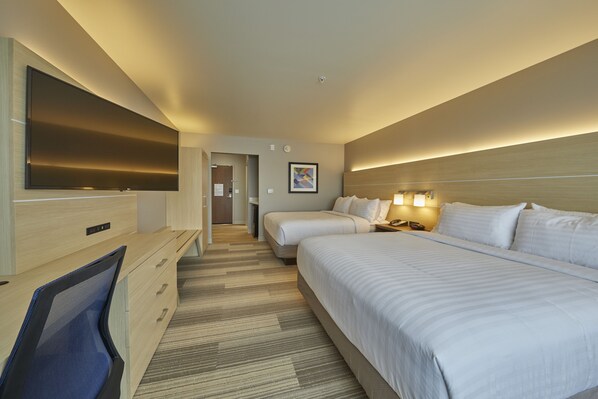 Habitación de hotel con una televisión de pantalla plana grande, dos camas, un escritorio con una silla y un cabecero con iluminación integrada.