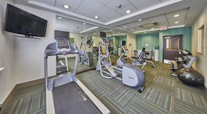 Gimnasio de hotel con cintas de correr, elípticas y pesas libres.