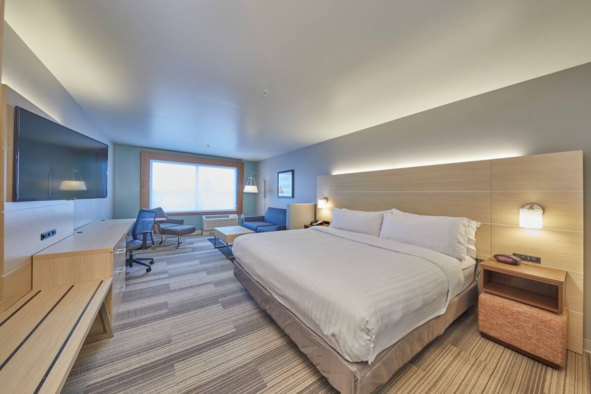 A modern hotel room with a large bed, a desk, a chair, and a TV.