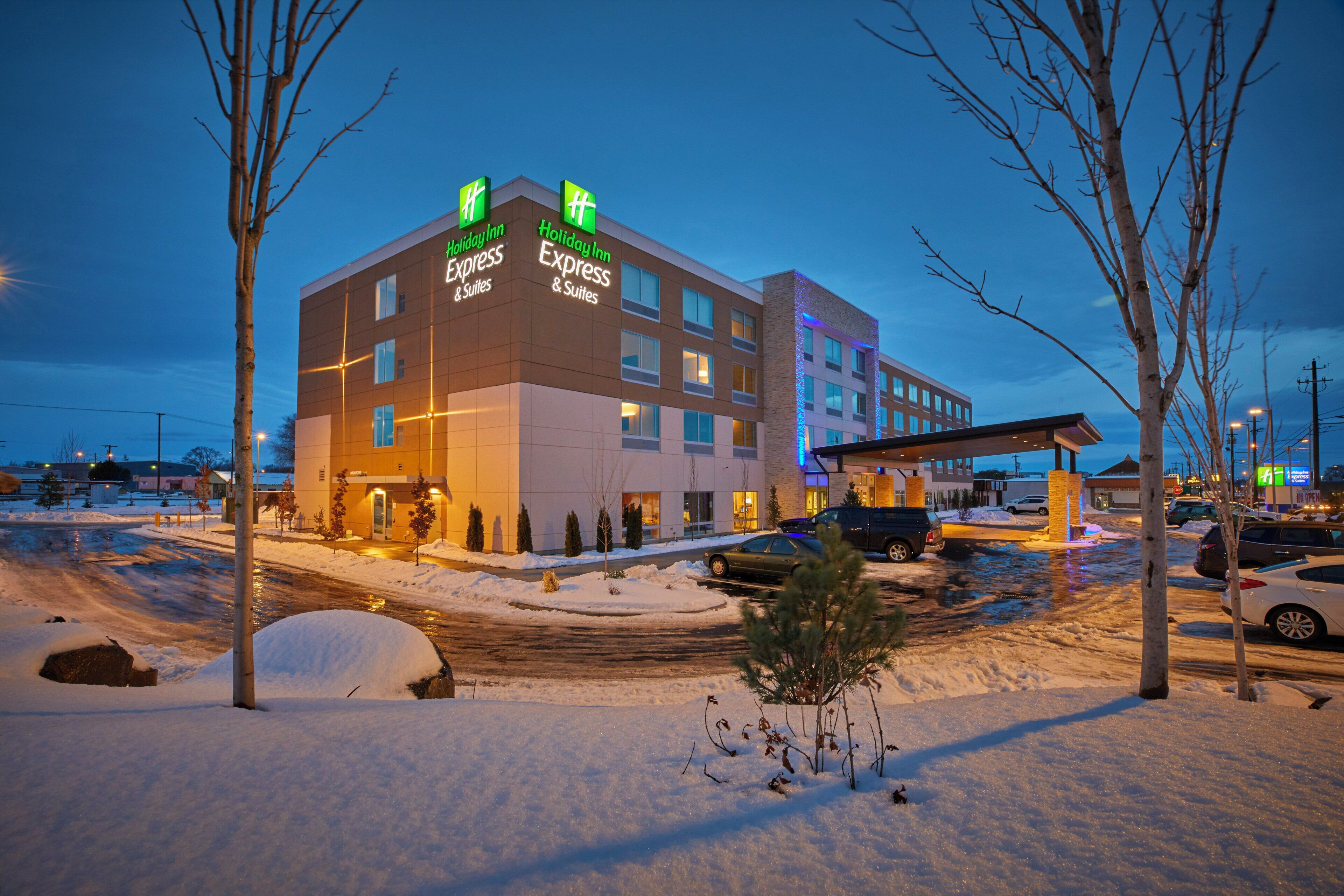 A Holiday Inn Express & Suites building with a snow-covered parking lot and bare trees.