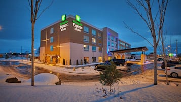 Edificio de Holiday Inn Express & Suites con un estacionamiento cubierto de nieve y árboles sin hojas.