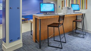 A reception desk with two monitors, a printer, and a keyboard. There are two chairs and a small table with a bench. The room has a blue accent wall and a carpeted floor.