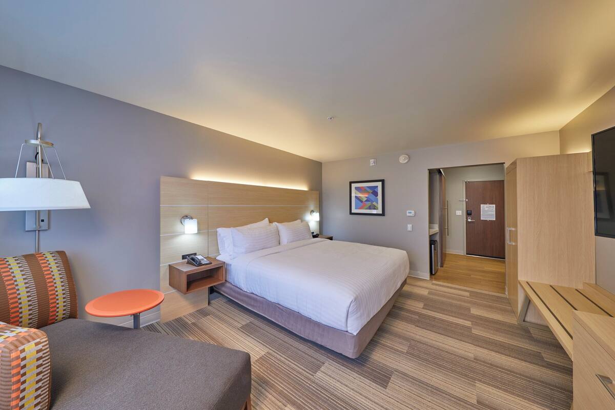 A hotel room with a large bed, a desk, a chair, a small table, and a TV.