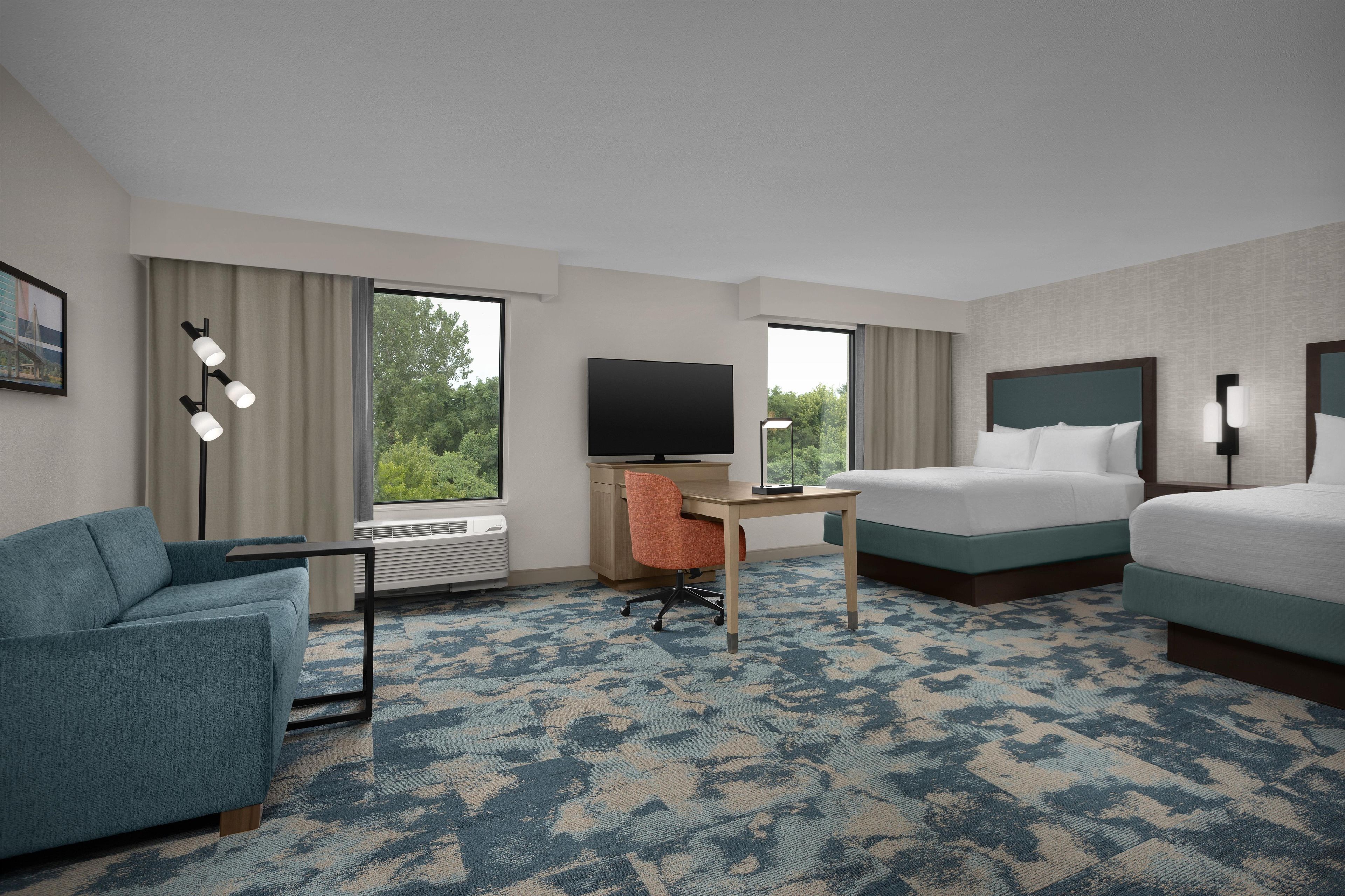 A hotel room with a bed, a desk with a chair, a sofa, and a television.