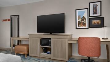 A hotel room with a flat-screen TV, a desk, a chair, and a bed.