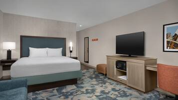 A hotel room with a bed, a desk with a flat-screen TV, a chair, a nightstand, and a wall-mounted TV.