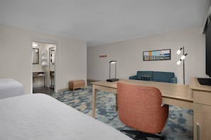 Une chambre d’hôtel avec un lit, un bureau, une chaise, un canapé, une télévision, une lampe et un tableau au mur.