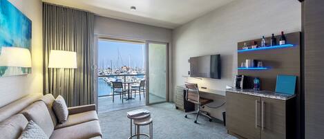 Habitación de hotel moderna con sofá, escritorio, televisión y balcón con vista al puerto deportivo.