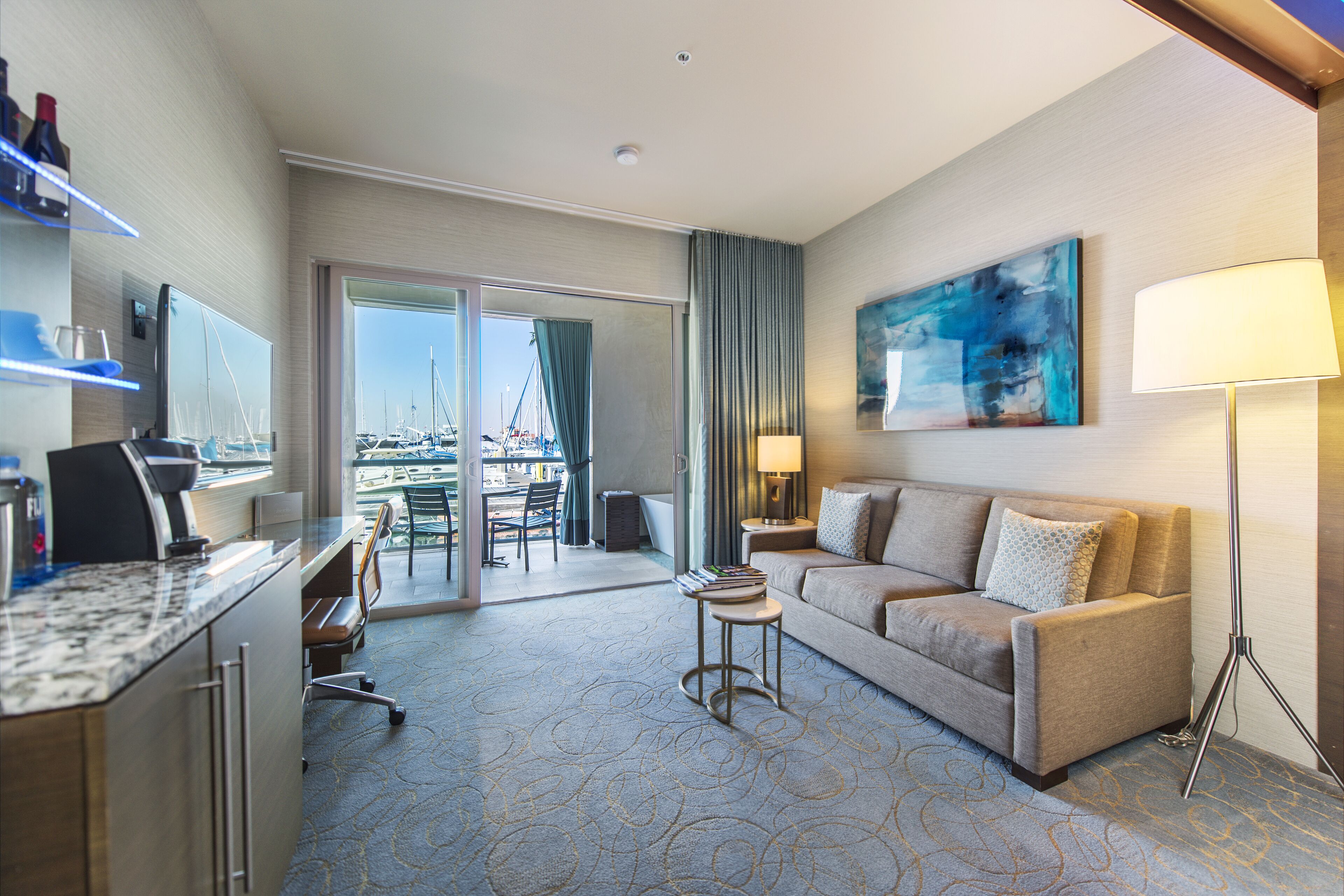 A hotel room with a desk, a sofa, a lamp, and a painting on the wall.