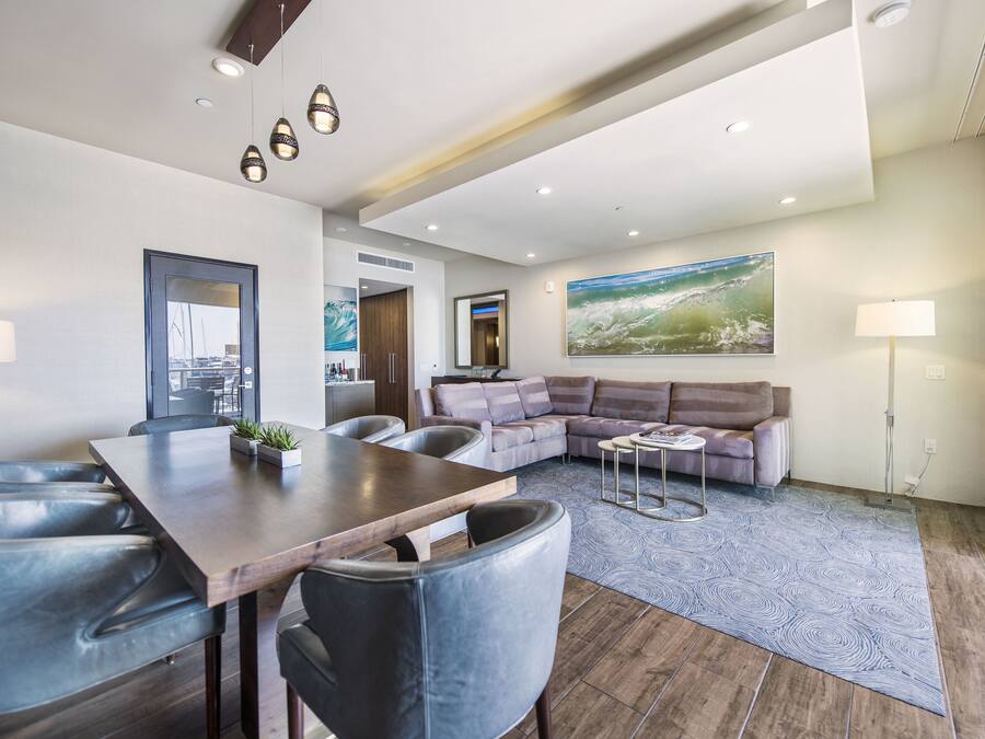 A modern living room with a wooden dining table, leather chairs, a sectional sofa, and a large abstract painting on the wall.