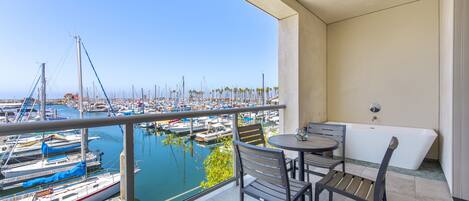 A balcony with a view of a marina, a table with chairs, and a bathtub.