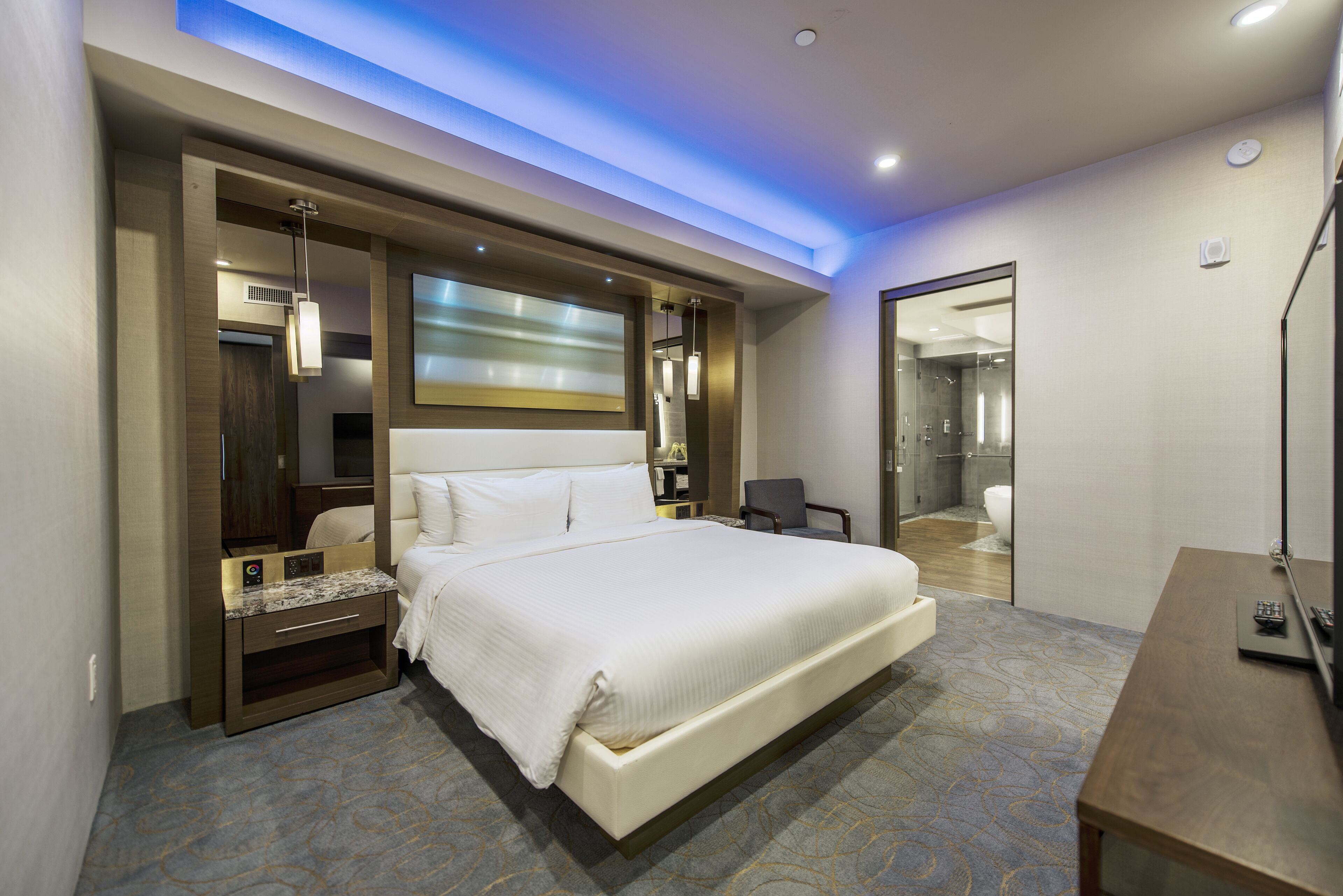 Een moderne hotelkamer met een groot bed, een bureau, een stoel en een zichtbare badkamer door een glazen deur.