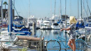 A person standing next to a bicycle at a marina with boats in the background.